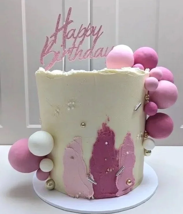 Beautiful ivory buttercream covered birthday cake with white and pale pink spheres, pink buttercream palette detailing, and edible pearls. Topped with a pastel pink Happy Birthday cake topper.
