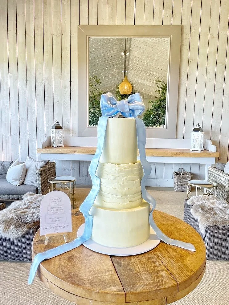 Elegant, modern,  tall, layered ivory buttercream wedding cake with a large blue satin bow. Venue: Primrose Hill Farm, Warwickshire.