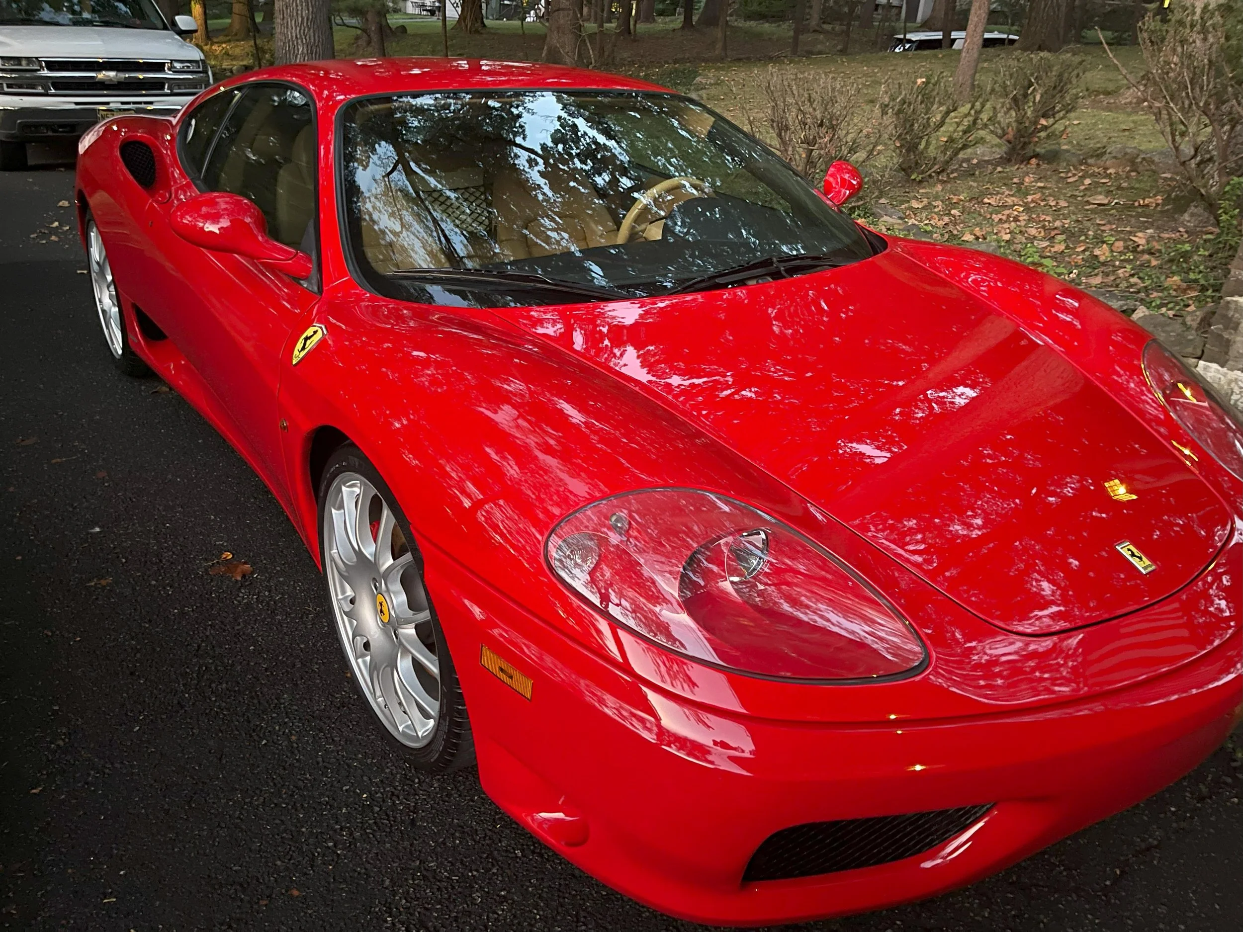 A red Ferrari sports car parked outdoors on a paved surface next to trees and bushes with a black mesh grille visible through the windshield.