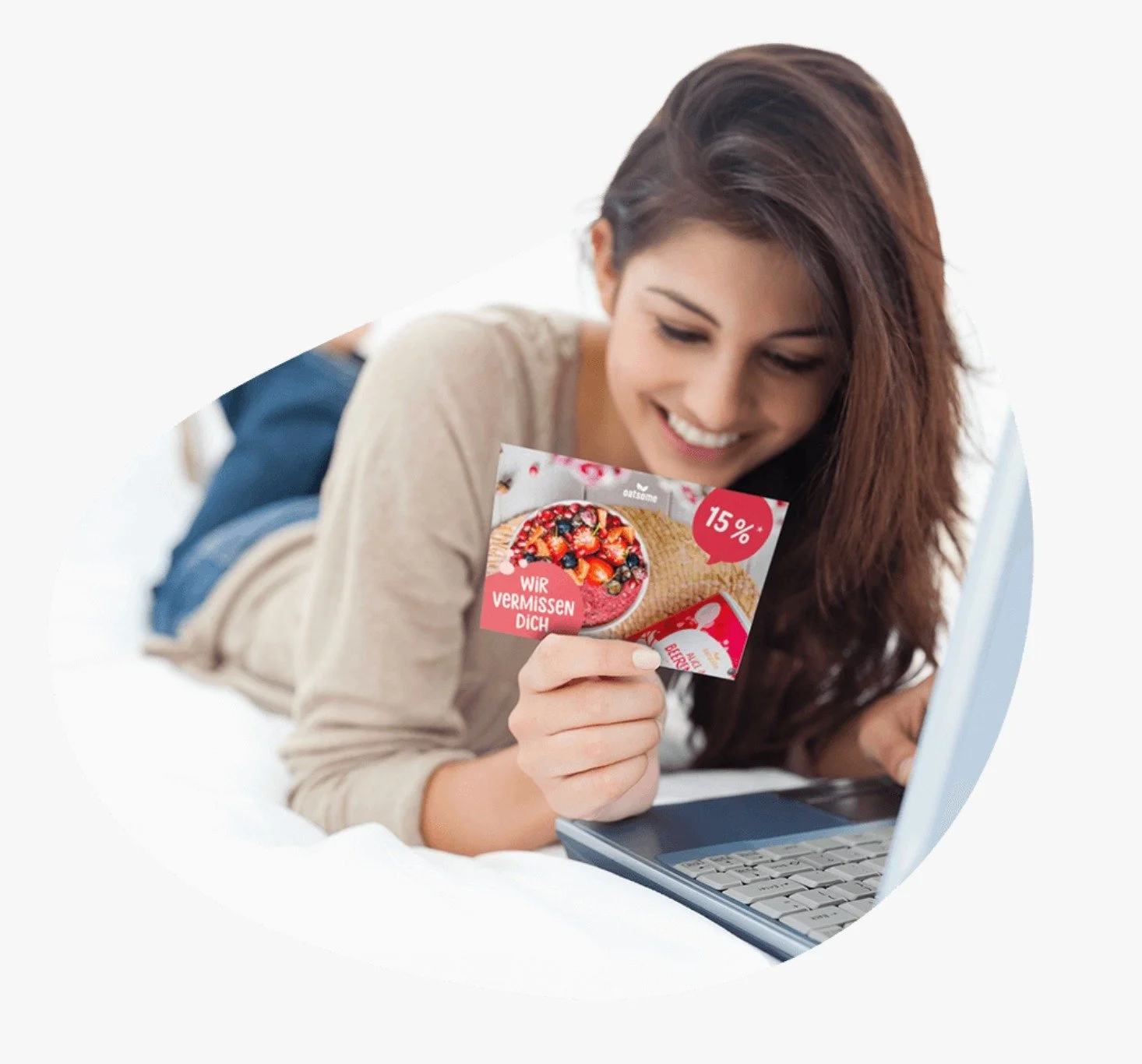 Junge Frau liegt auf einem Bett, schaut auf ihren Laptop und hält eine Werbekarte für ein Fruchteis mit dem Text "Wir vermissen dich" in der Hand.