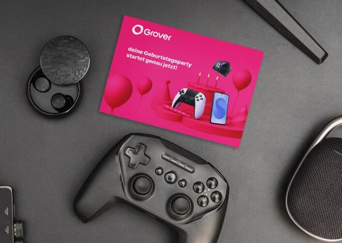 Werbegutschein für Grover mit Gaming-Controller, Kamera, Smartphone und Ballons auf einem Tisch.