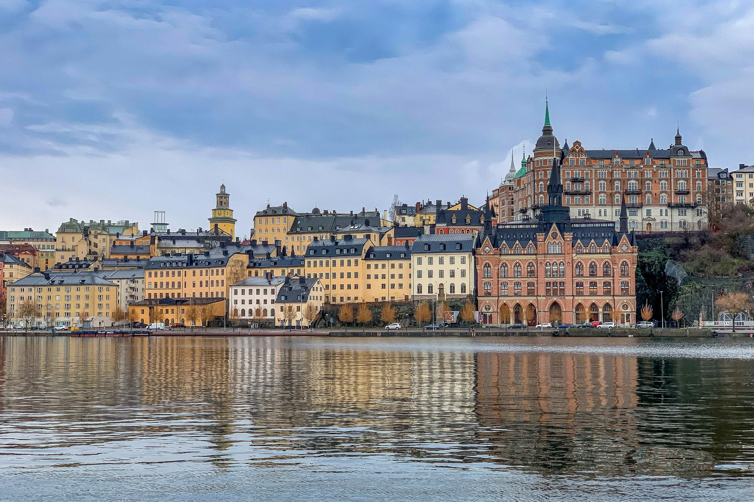 A scenic view of a European city skyline with historic buildings reflecting on a river, under a partly cloudy sky.