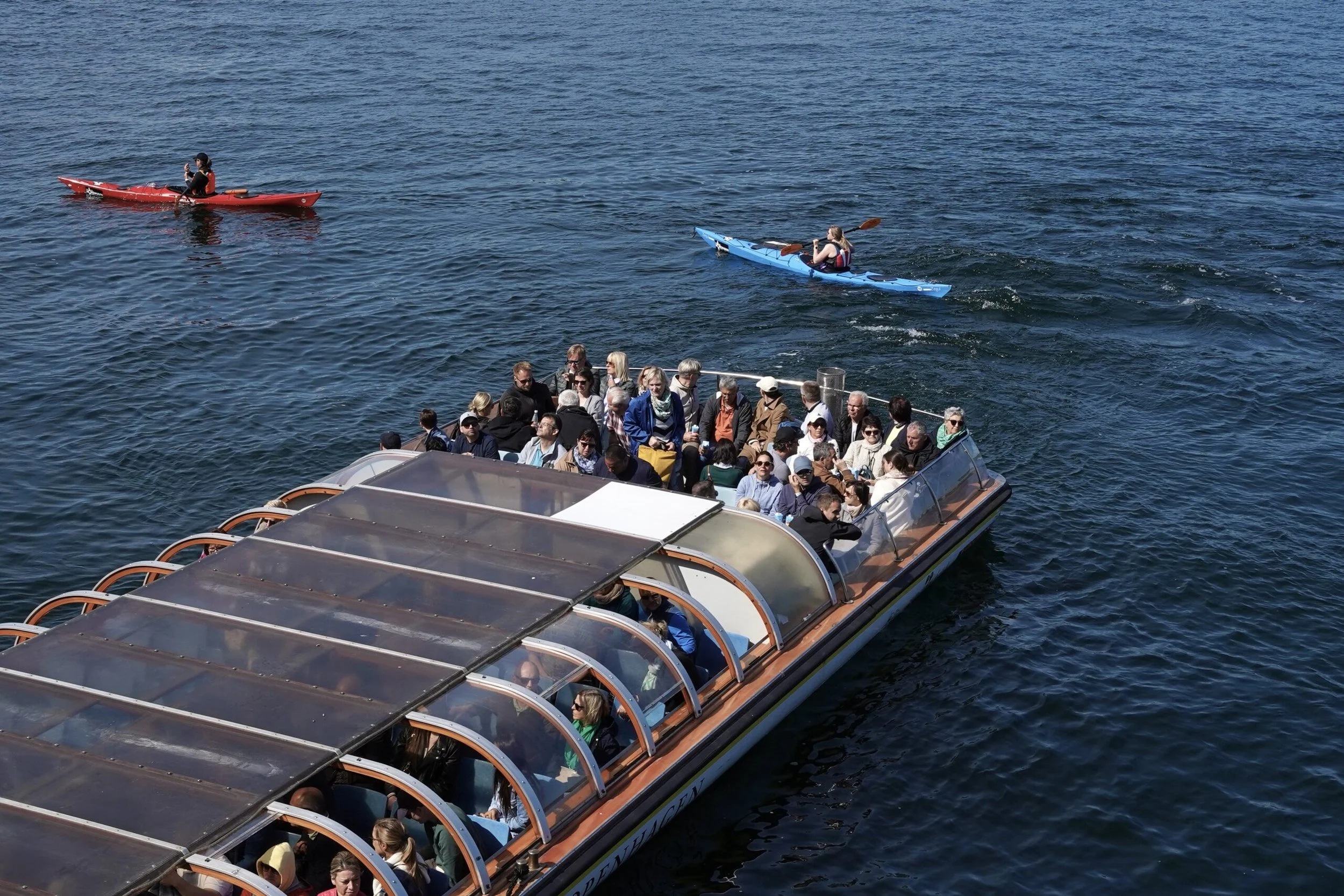 Tourist boat filled with passengers in the water, with two people kayaking nearby.