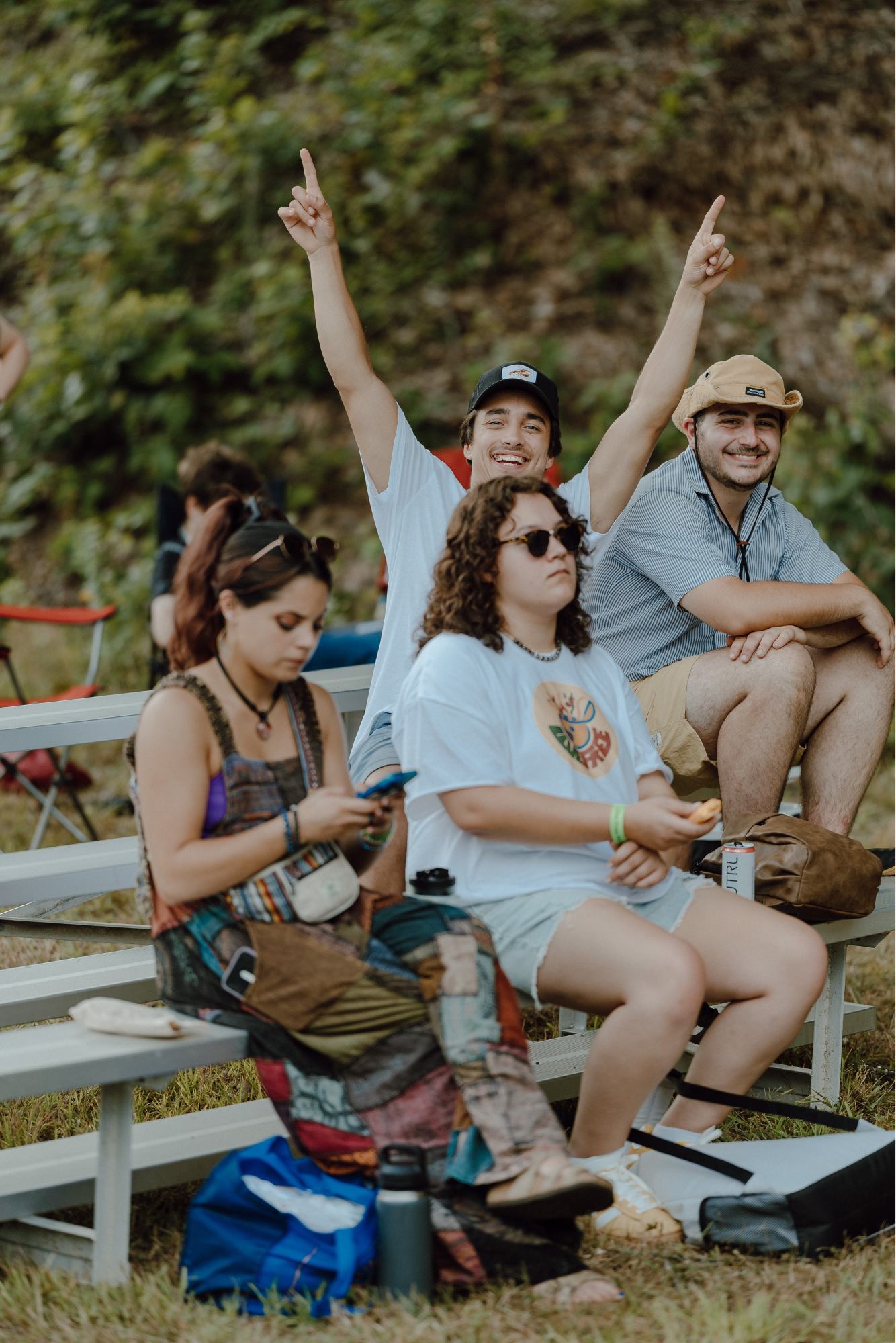 A group of young people sitting on park benches outdoors, with one man smiling and raising his arms in the air.