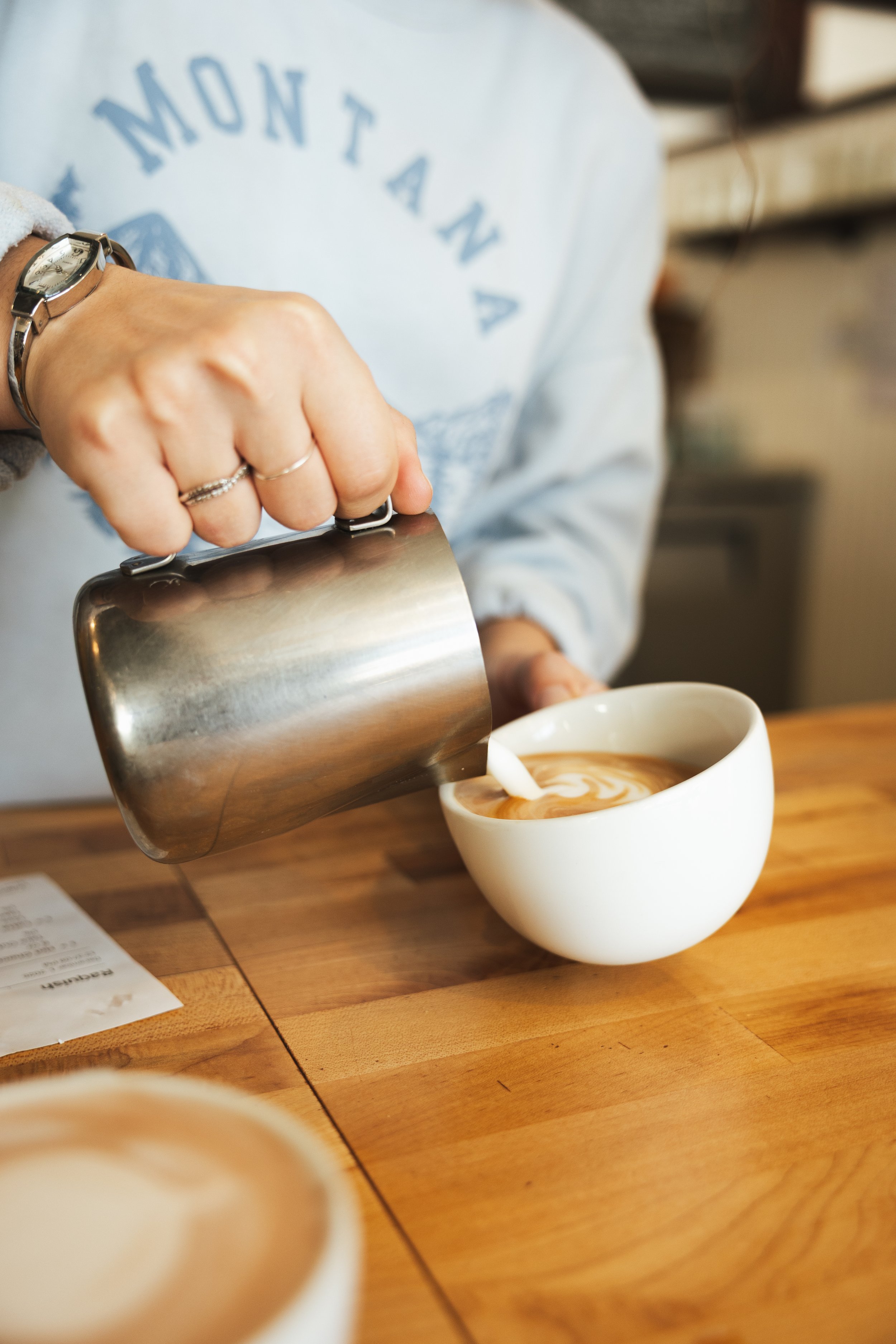 Person pouring milk into a cup of coffee with latte art.