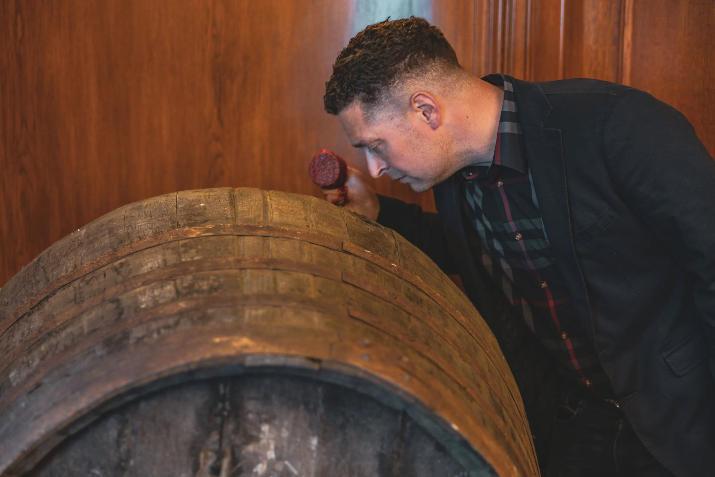 A man smelling whisky maturing in a wooden barrel.