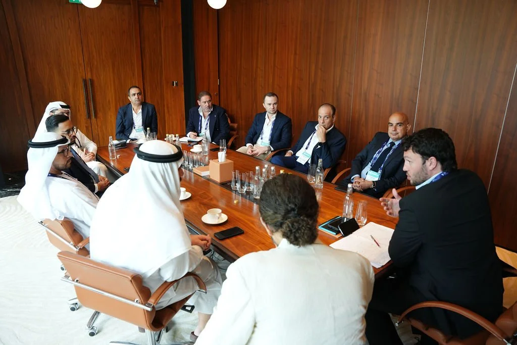 Business meeting with professionals in a conference room, seated around a large wooden table, engaging in discussion.