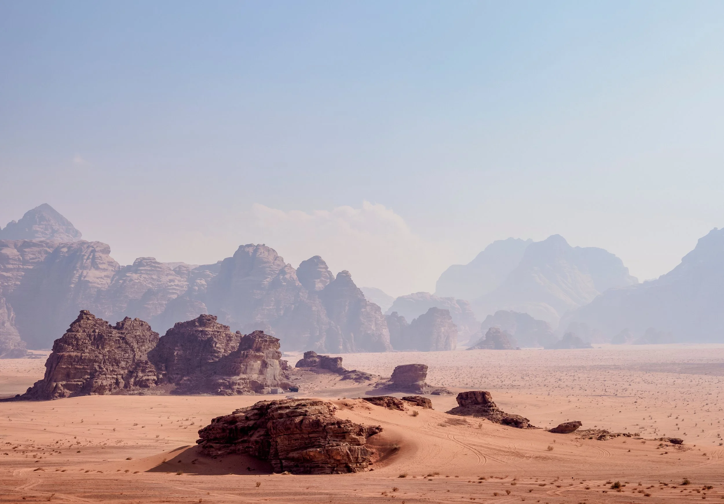 A desert landscape with rocky formations, sandy terrain, and distant mountains under a clear blue sky.