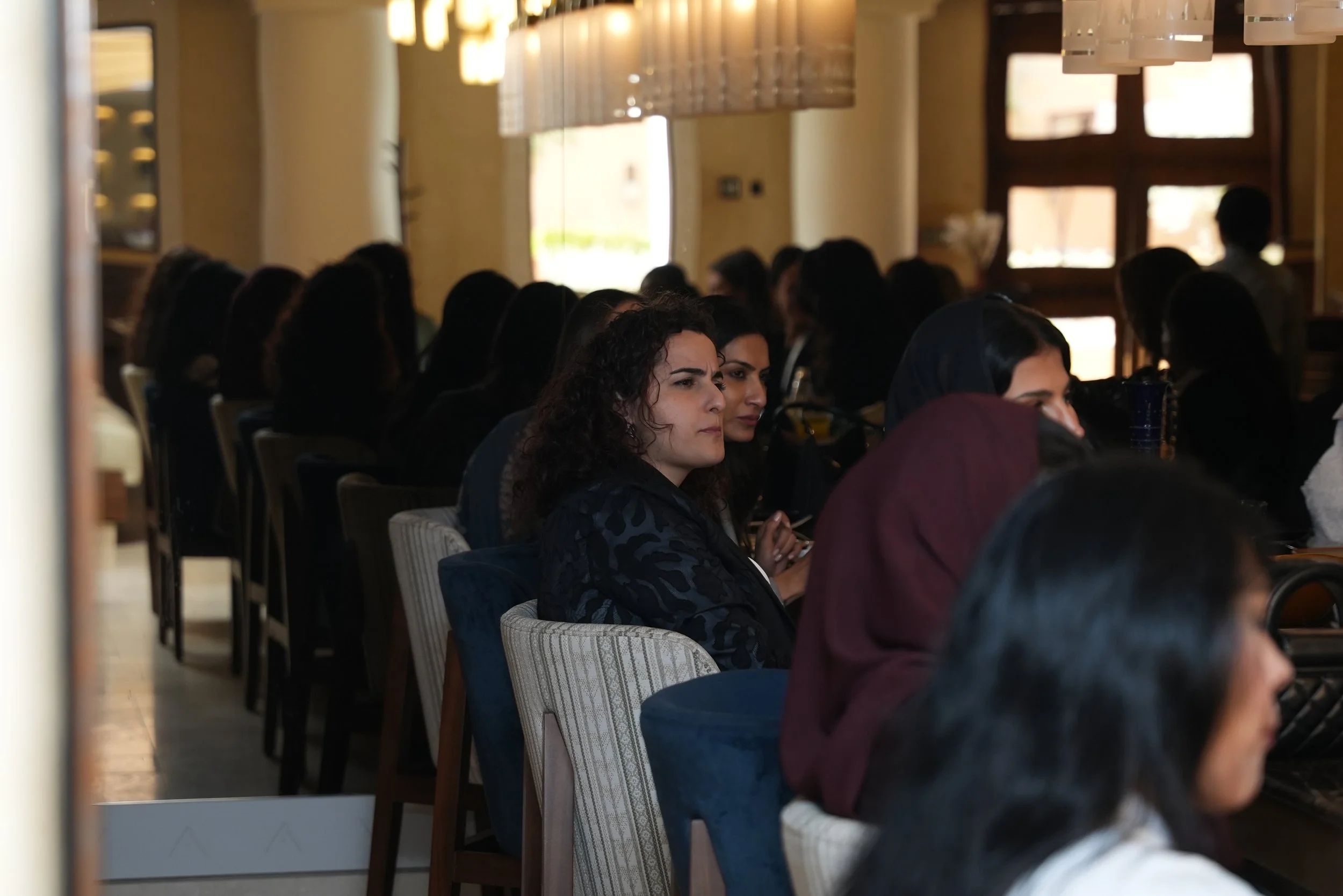 Women seated in rows at an indoor event, listening attentively.