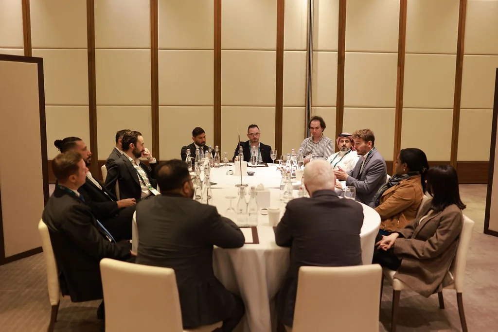 A group of people sitting around a round dining table in a conference room, engaged in a meeting or discussion.