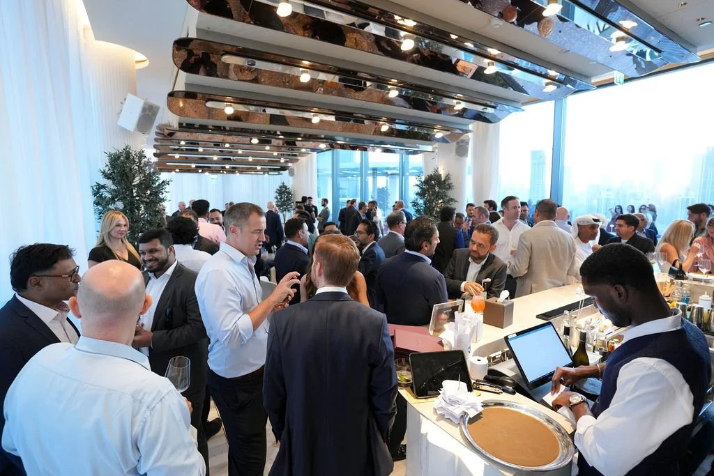 People mingling at a professional networking event or conference indoors with large windows and modern decor.
