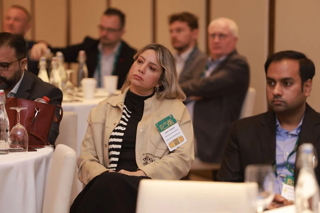Attendees sitting at a conference table listening to a presentation, with water bottles and glasses on the table.