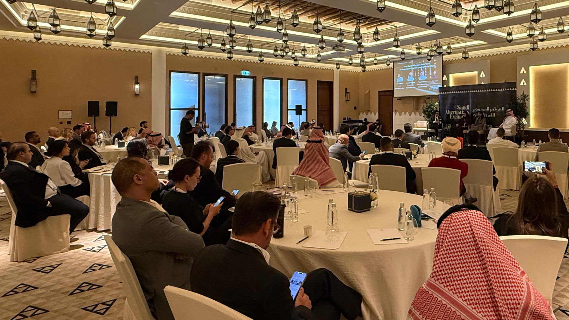 Attendees seated at round tables in a conference room listening to a panel discussion at the Diplomatic and Consular Exposition.