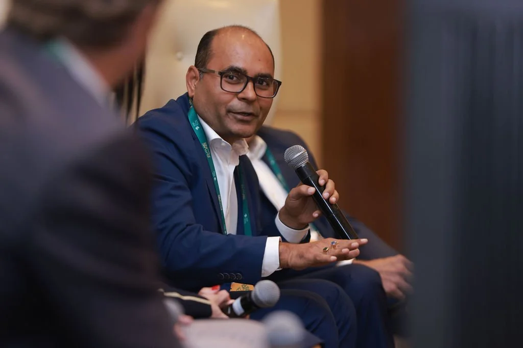 Man in a navy suit and glasses speaking into a microphone during a panel discussion.