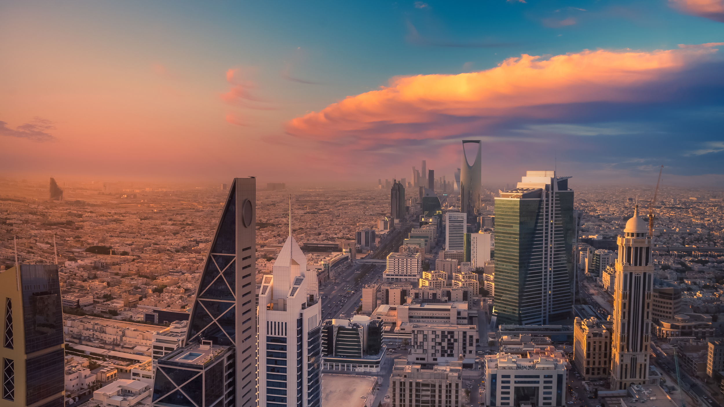 Skyline of a city with tall skyscrapers during sunset, with pink and orange clouds in the sky.