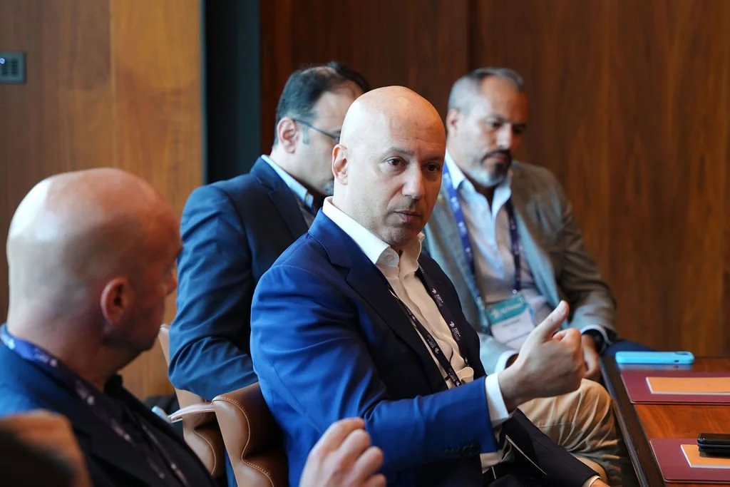 Four men in business attire sitting at a conference table, one of them giving a thumbs-up gesture.