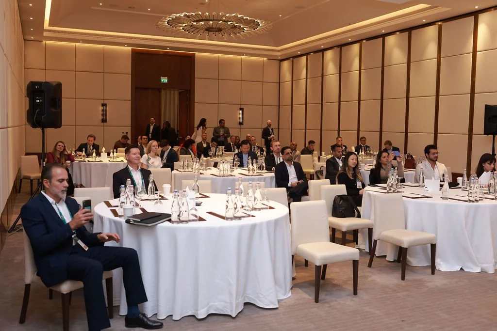 People seated at round tables in a conference room during a formal event or meeting.