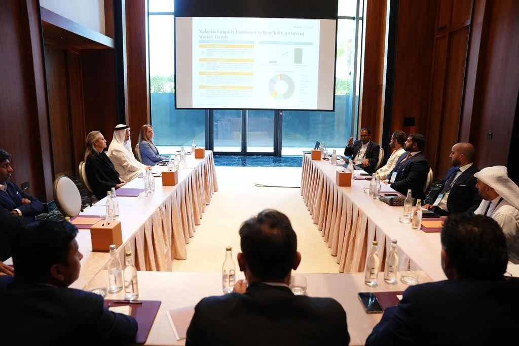 Business meeting with people seated around U-shaped table, watching presentation on screen in a conference room.