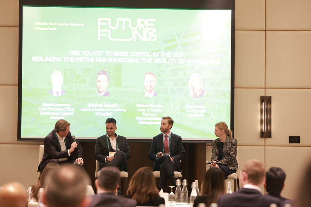 Four panelists seated on stage conducting a panel discussion at a conference, with a large green presentation screen behind them displaying the title "Future Funds" and information about the panelists.