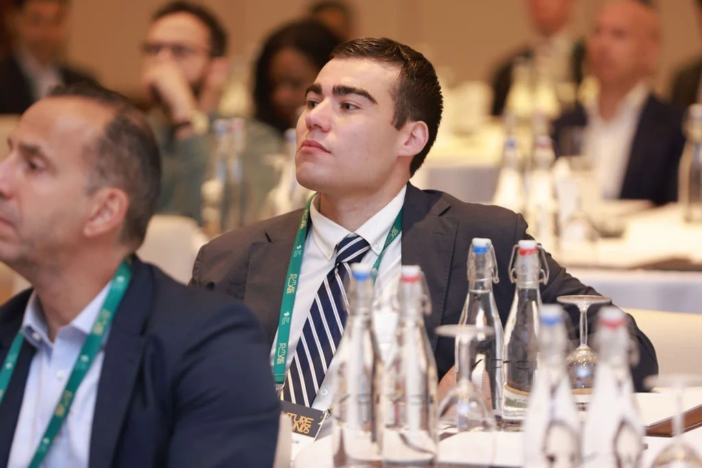 A young man in a business suit and striped tie attentively listening at a conference.