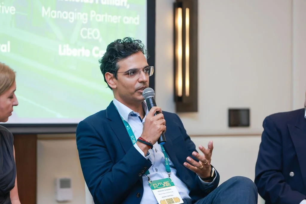 A man in a blue suit and glasses speaking into a microphone during a panel discussion at a conference.