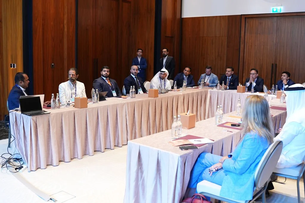 Business meeting with a U-shaped table in a conference room with multiple men and women seated, some taking notes, in formal attire.