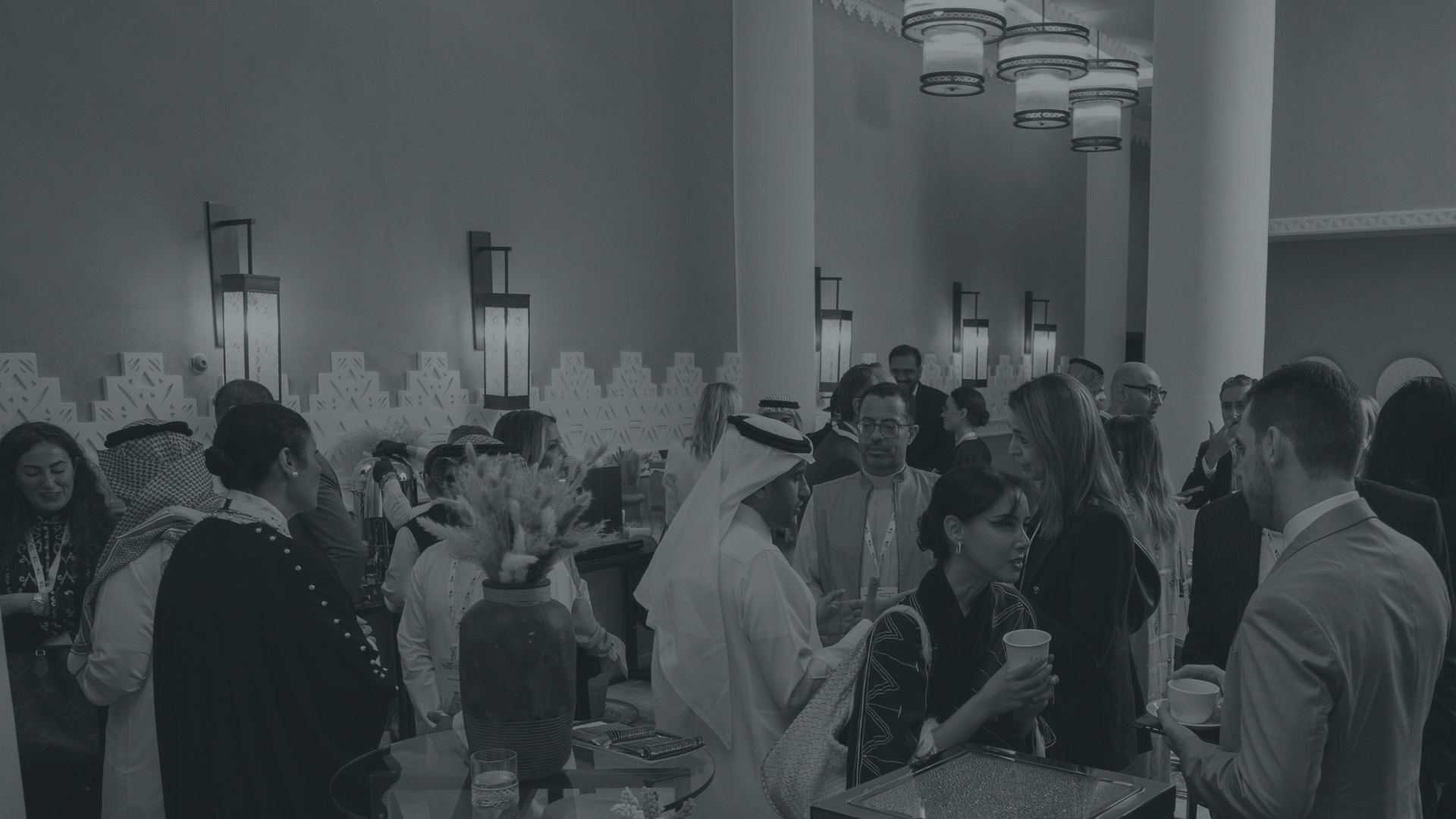 People gathered at a social event or conference, engaging in conversations. The venue has decorative wall lighting and modern interior design.