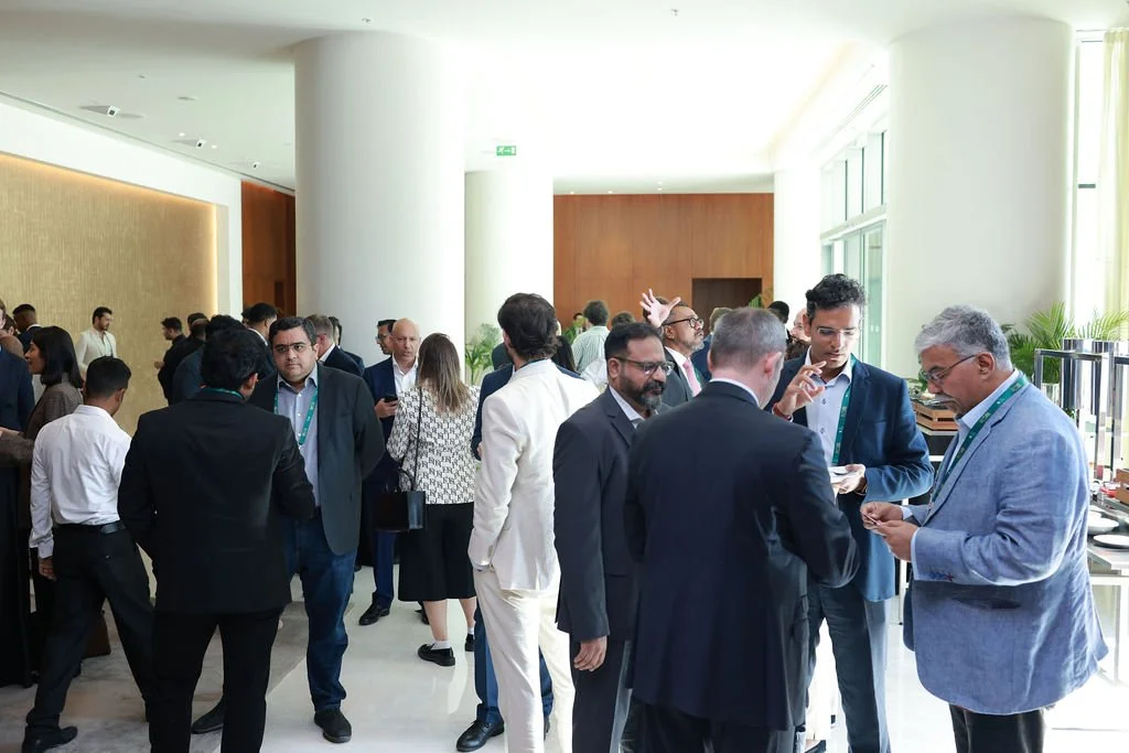 Business professionals at a networking event in a bright, modern conference space with large windows and white walls.