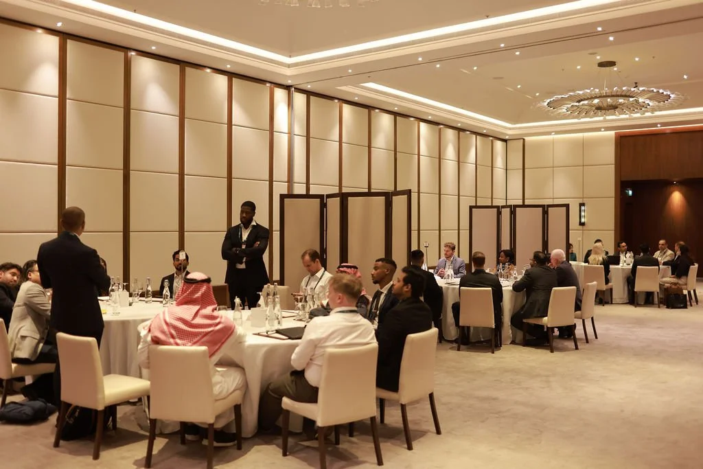Business conference with diverse attendees seated at round tables in a modern, well-lit banquet hall.