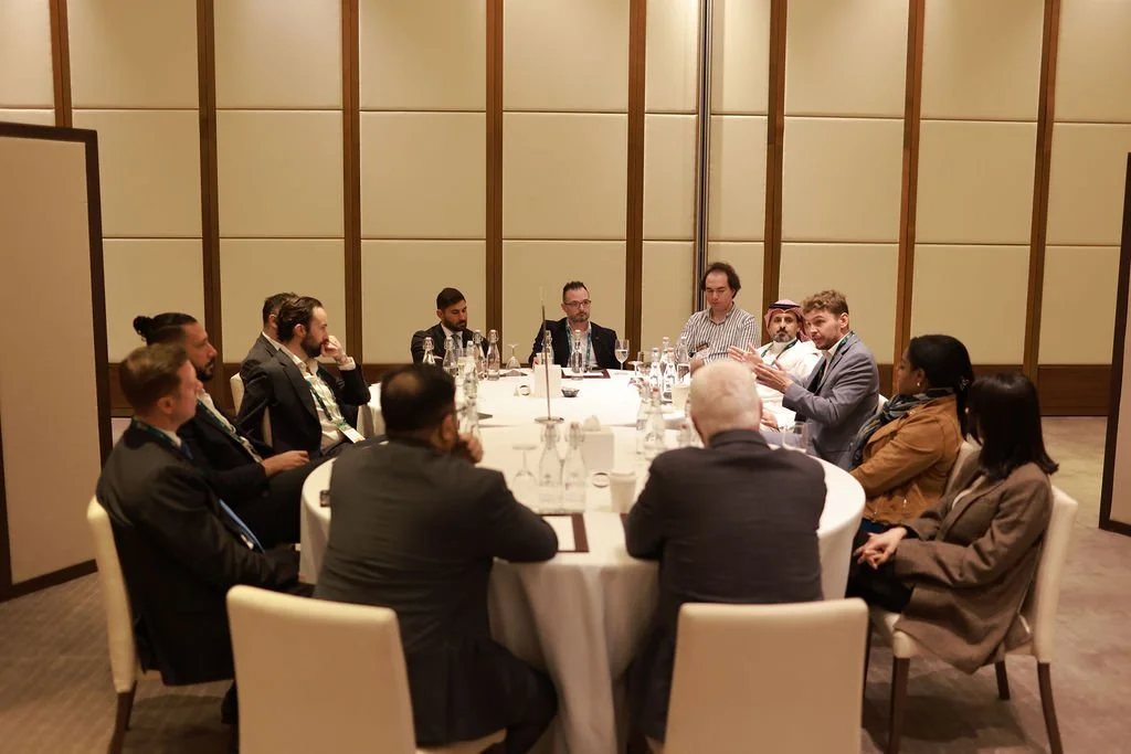 A group of people sitting around a round table in a conference room, engaging in a discussion.