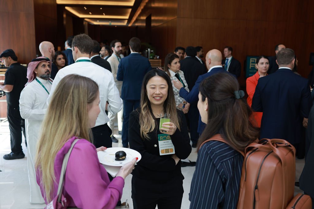 A group of diverse professionals at a conference or networking event, socializing and enjoying drinks in a modern indoor setting.
