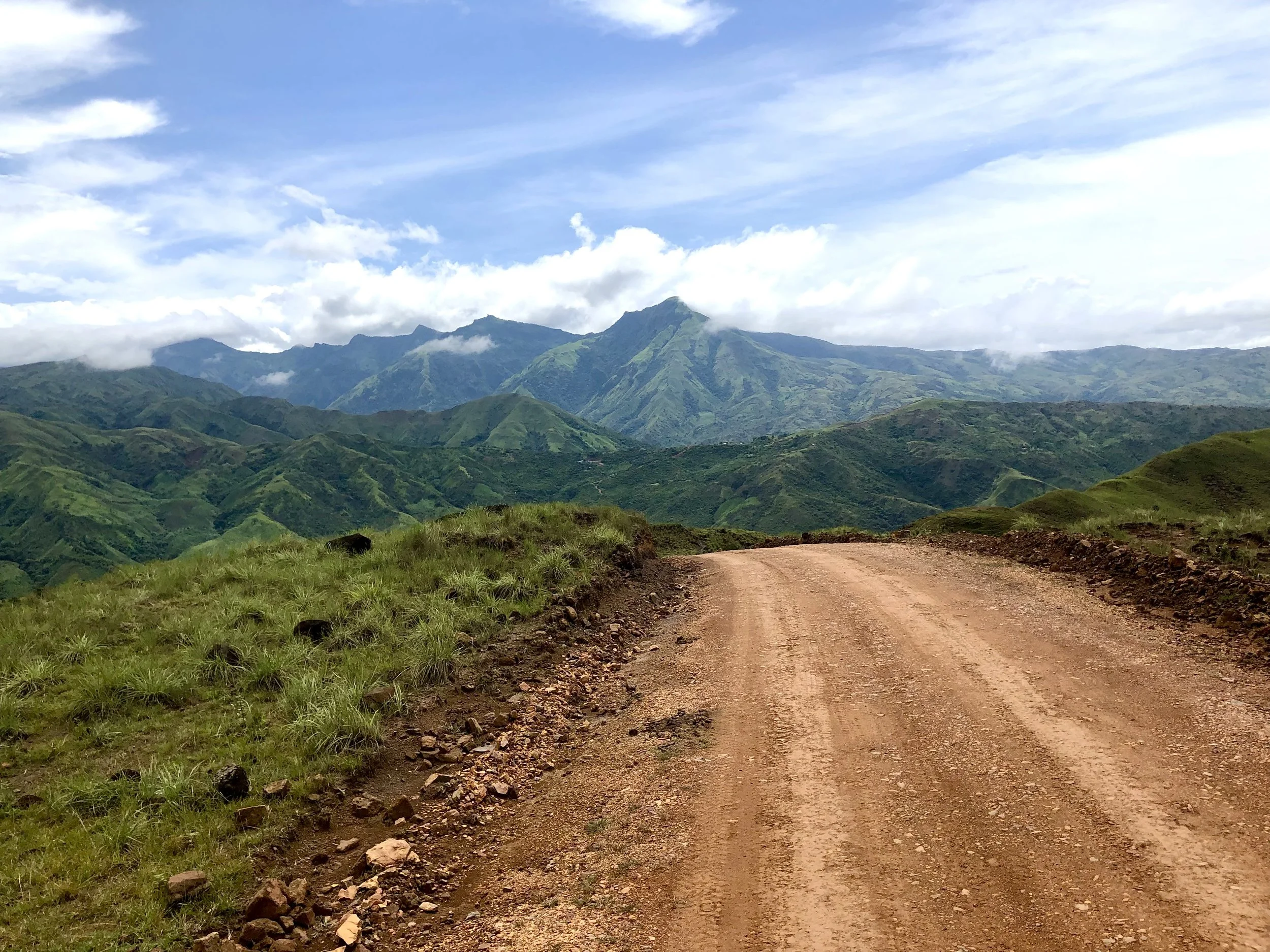 A dirt road winding through green hills with mountains in the background under a partly cloudy sky in Latin America. The road leads to a school where Danielle Shulkin led professional development for teachers and tutored students.