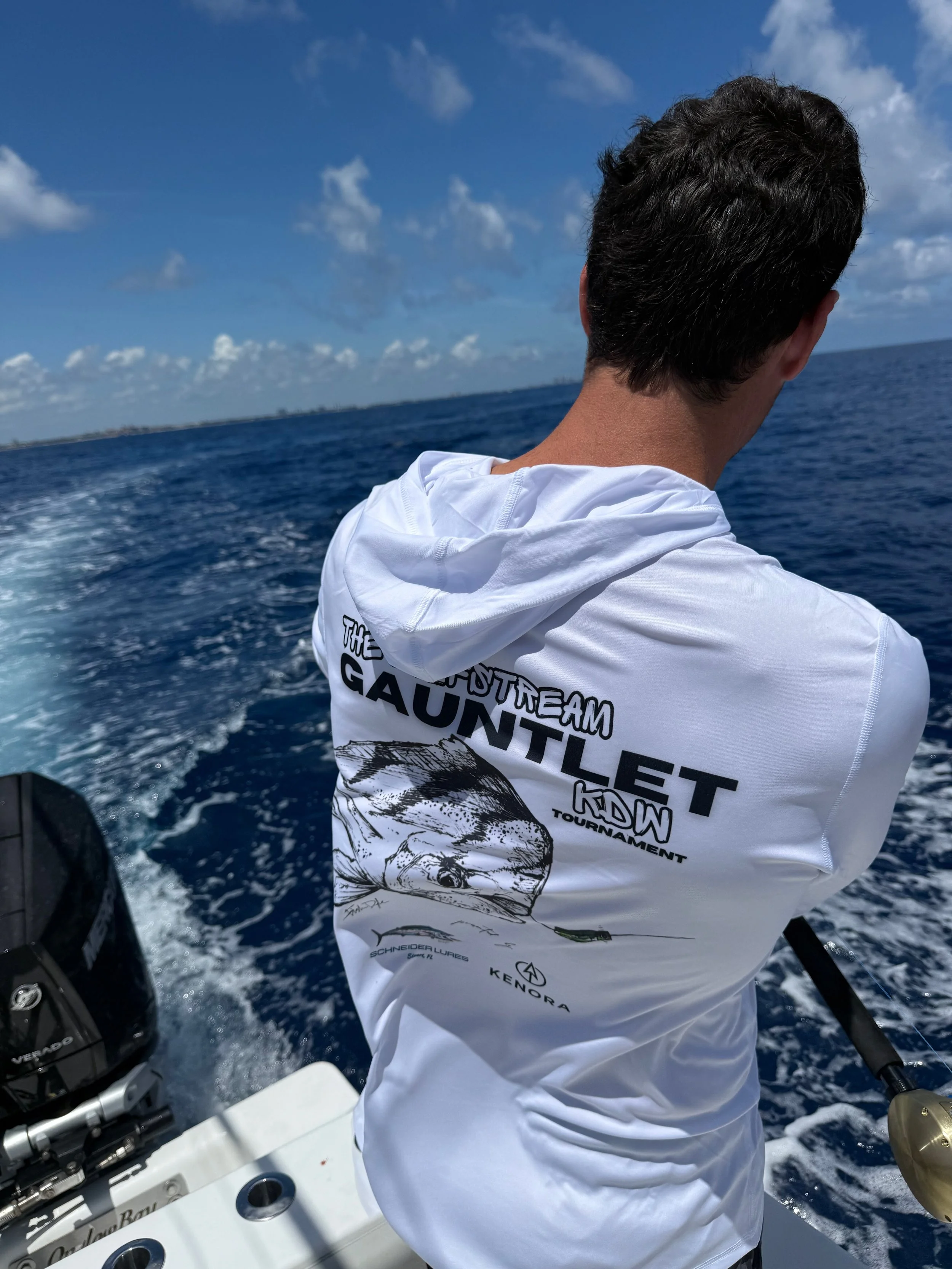 Tournament hoodie with graphic text and facing the horizon on a boat, with the ocean and blue sky with clouds in the background.
