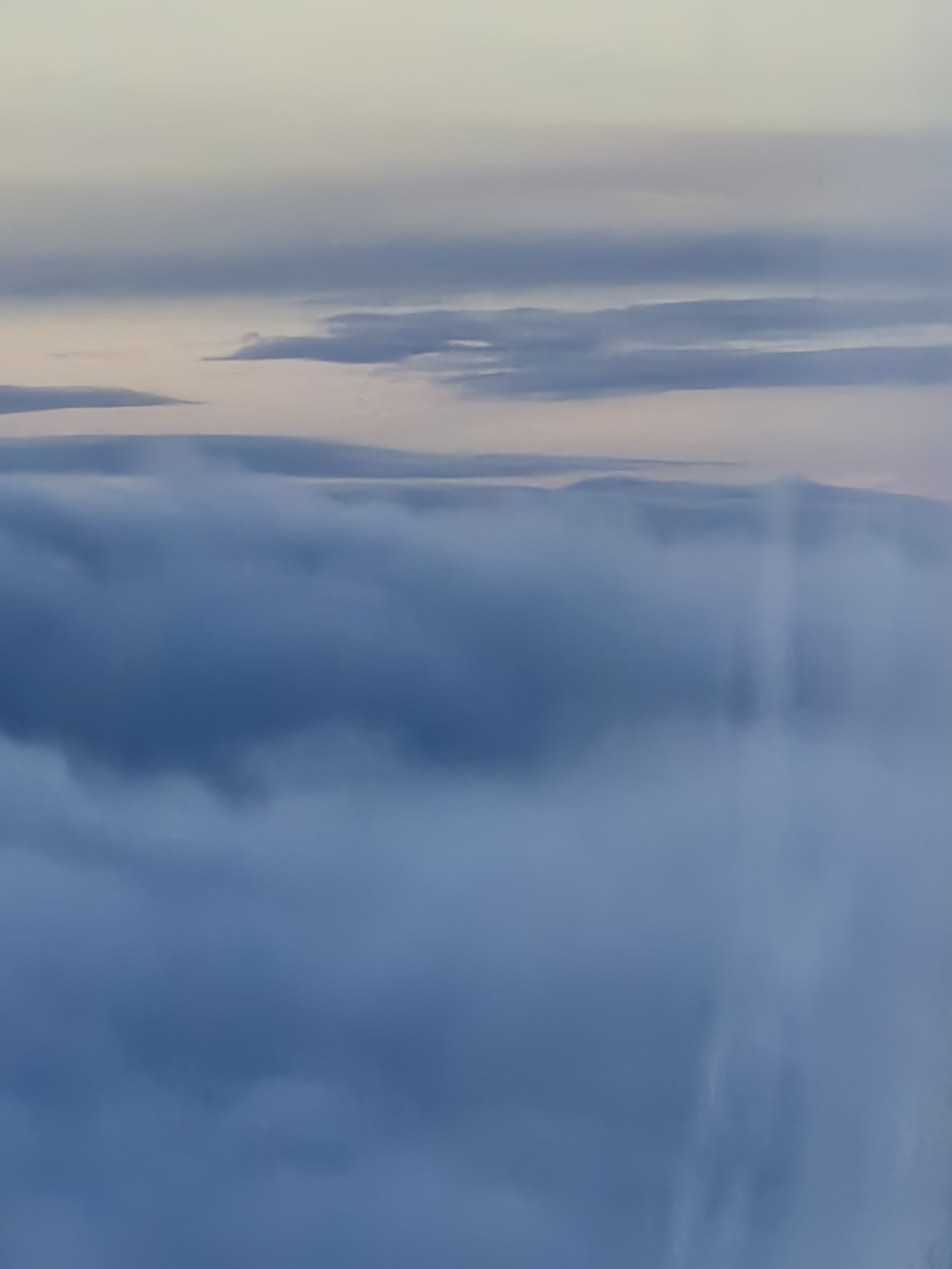 A view of a cloudy sky with various shades of blue and some darker, elongated clouds.