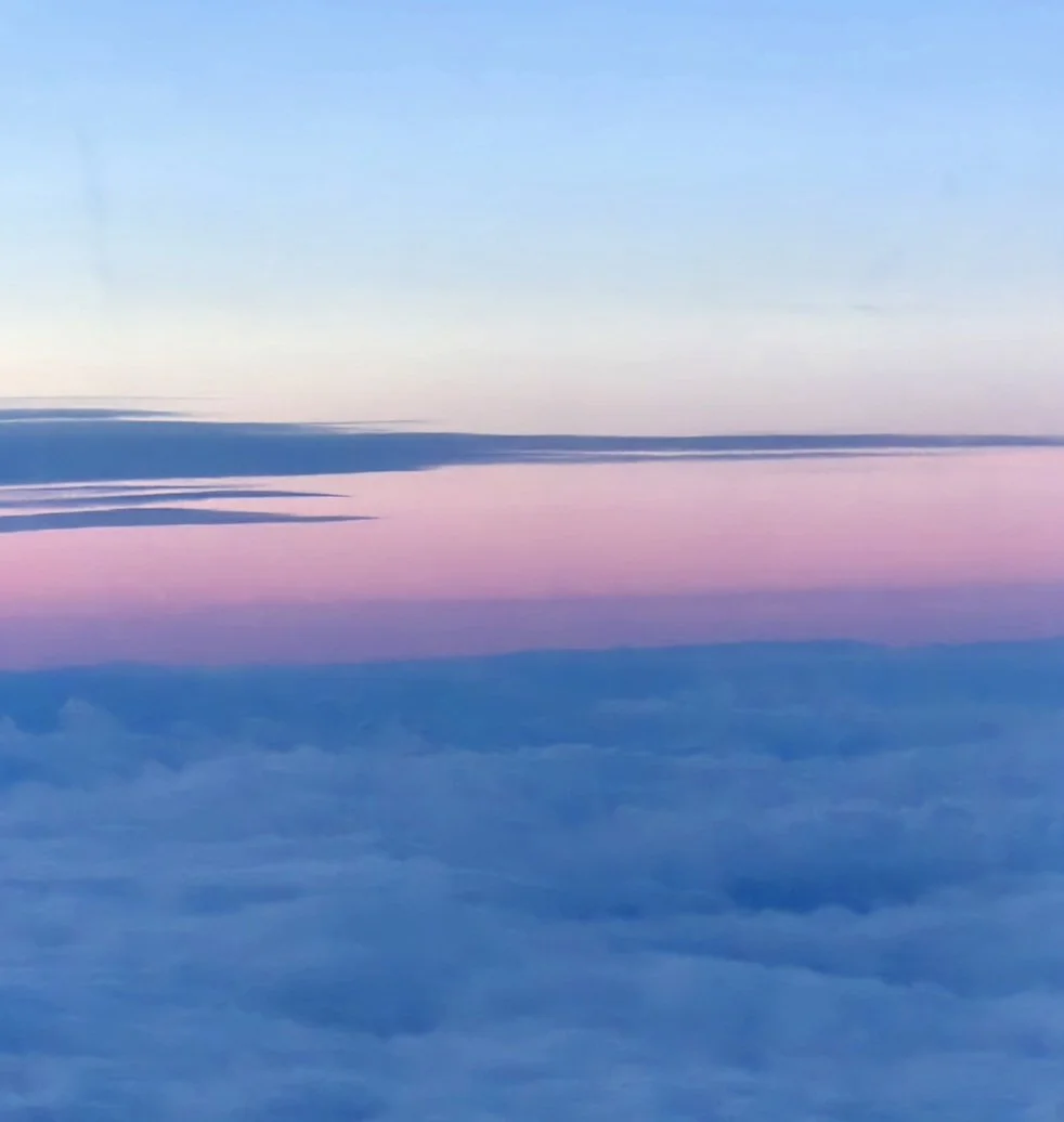 A view of a colorful sky with pastel pink, purple, and blue hues above clouds during sunset or sunrise.