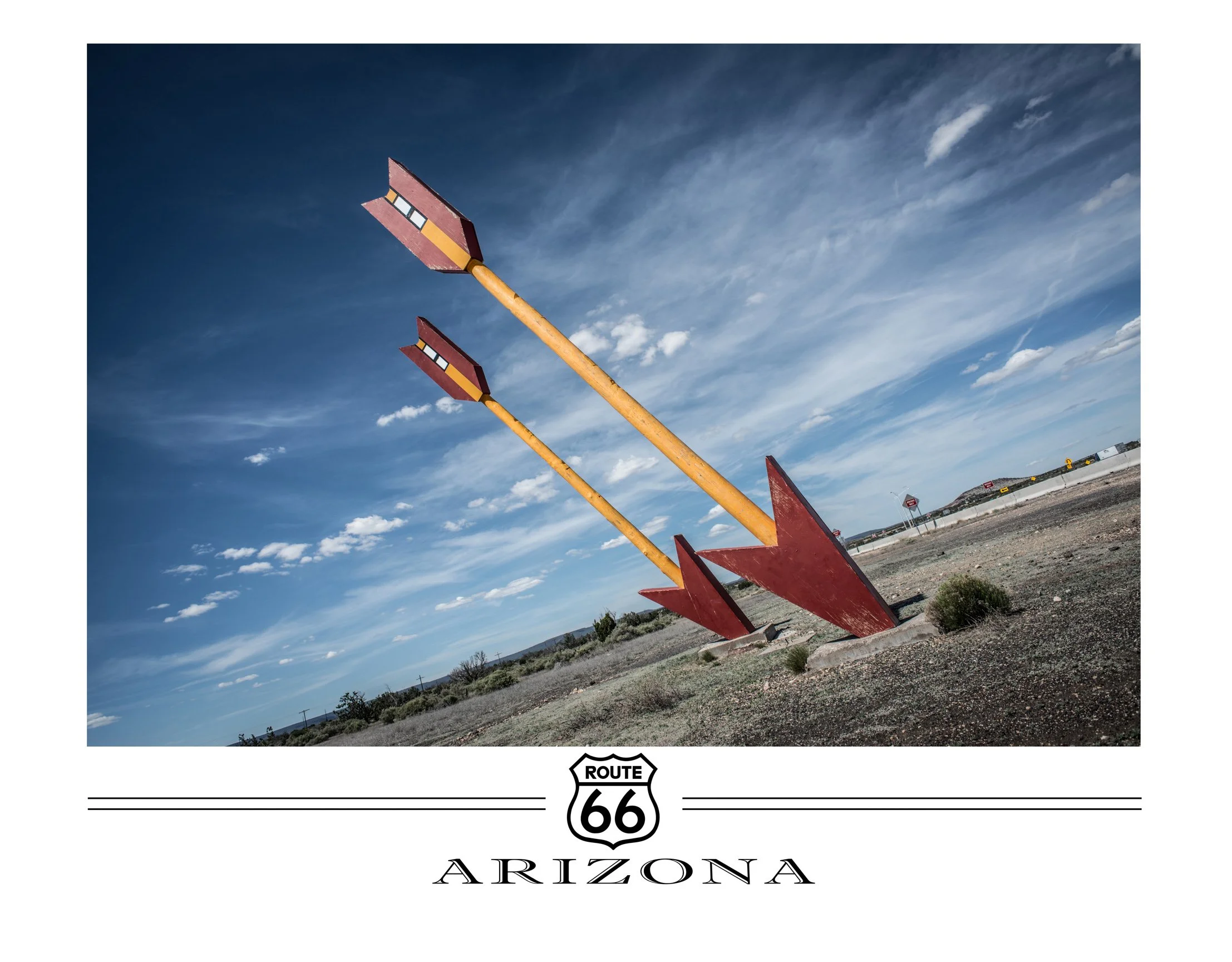 Two large, artistic sculptures of arrows on the ground in Arizona, under a blue sky with scattered clouds, with a Route 66 sign and state name at the bottom.