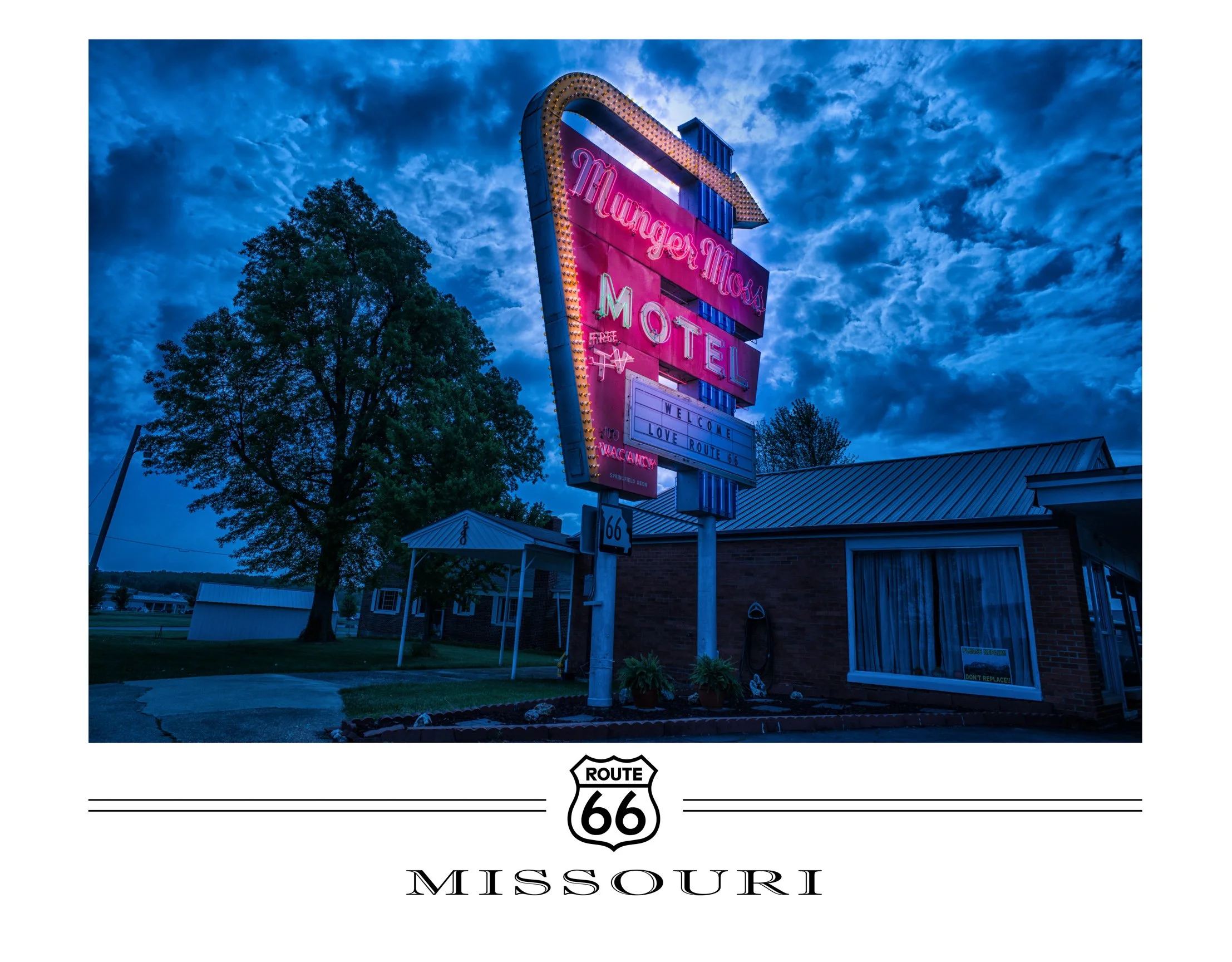 Bright neon sign for Mungers Motel on Route 66 at dusk, with a tree and a brick building around it.