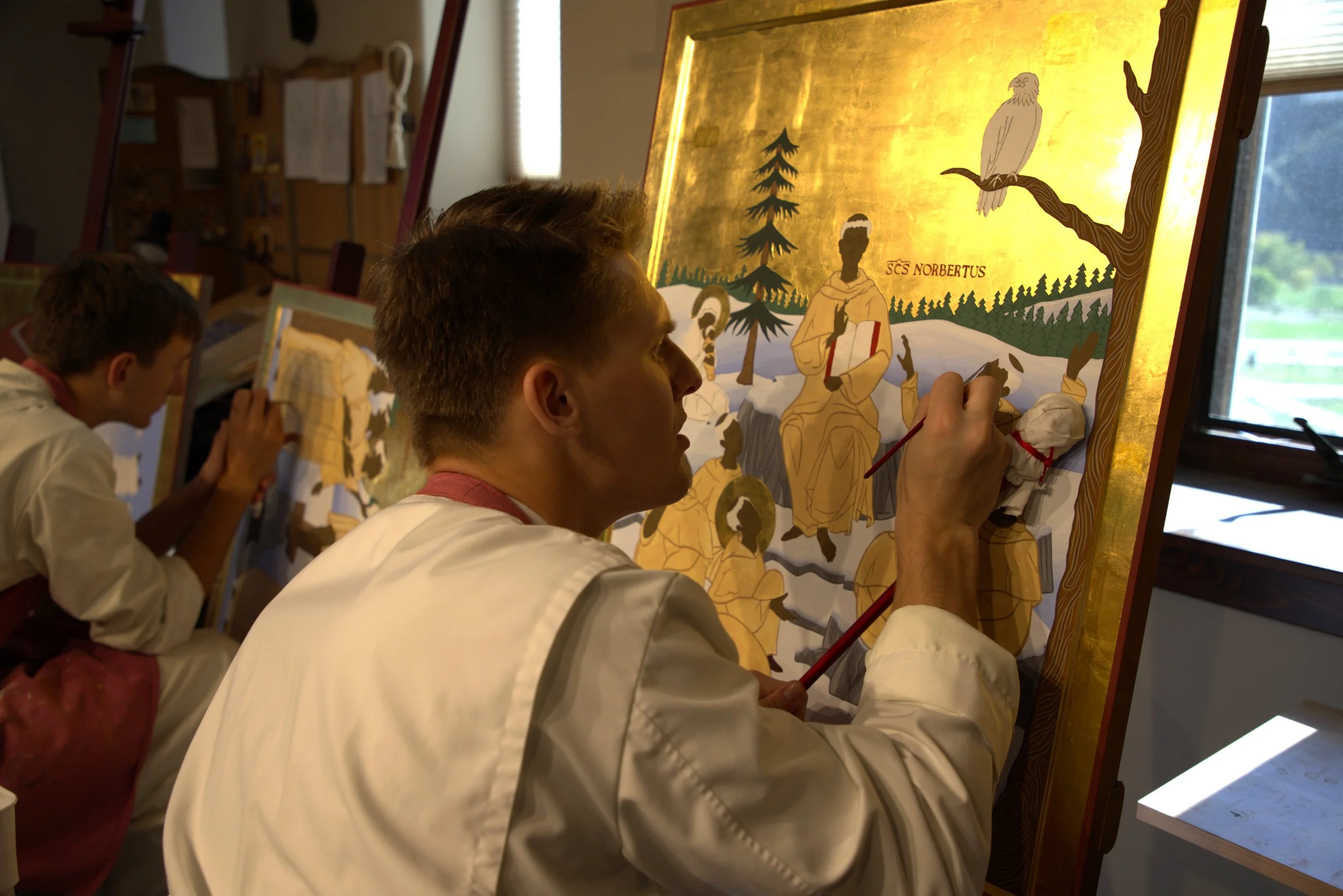 Jake Rogalski painting a religious icon on large wooden panels in an art studio.