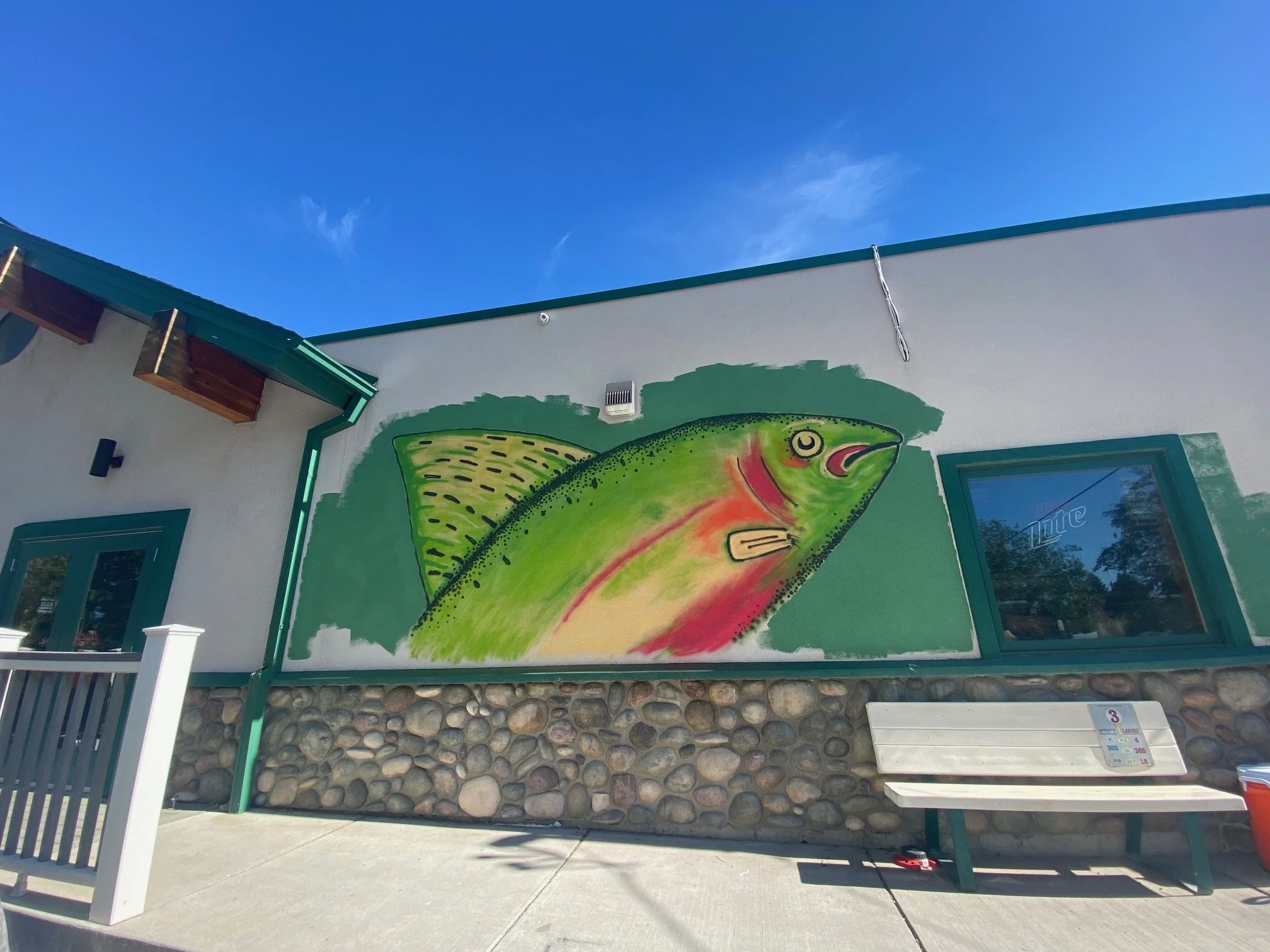A colorful mural of a fish painted on a white building wall under a clear blue sky.
