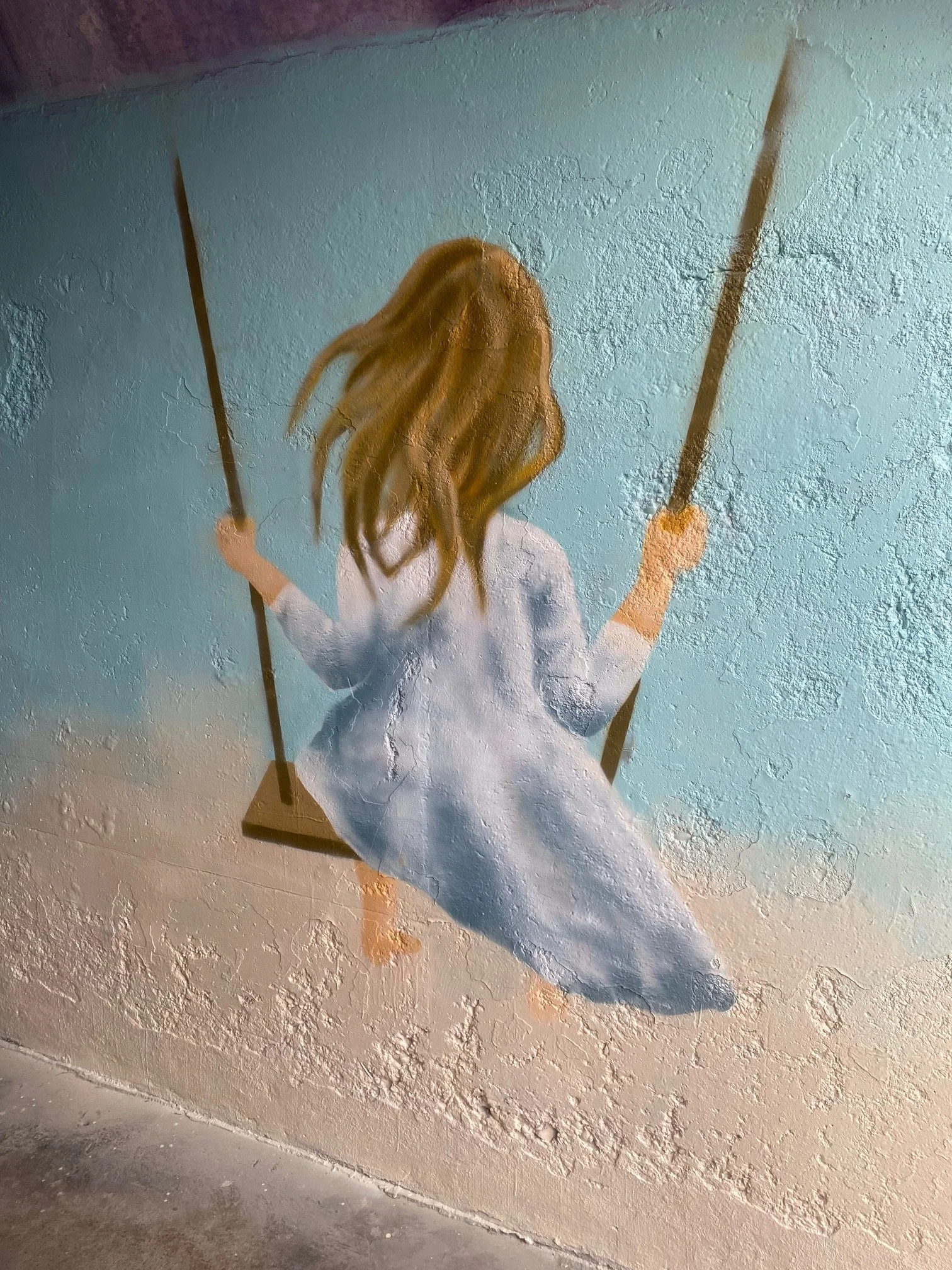 A mural of a woman with long hair holding a stick, painted on a textured wall.