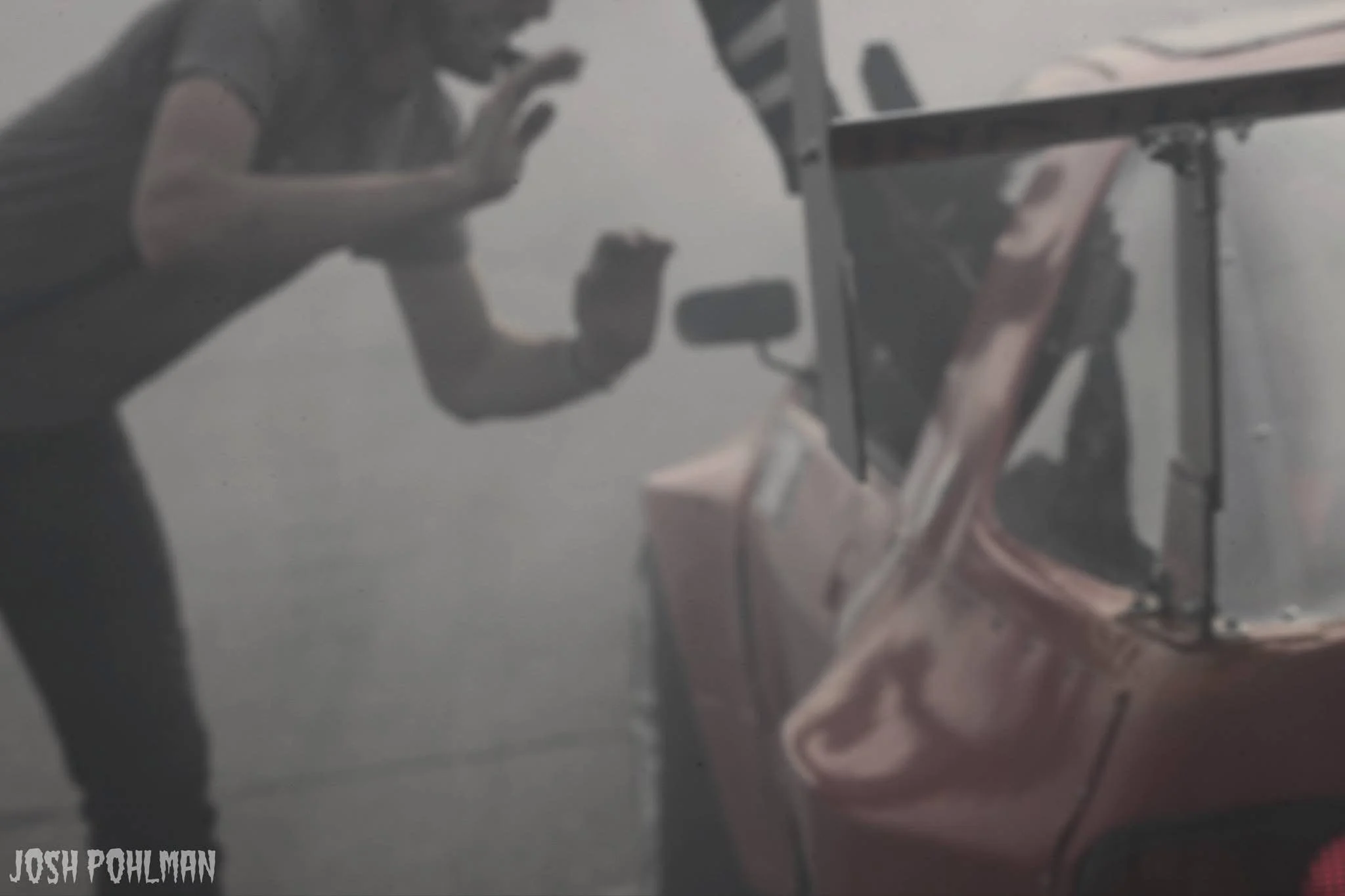 A person wearing a dark shirt is high fiving another person in a drift car after a a good run, with the focus on the man against a gray tire smoke filled background. The image has a soft, muted tone.