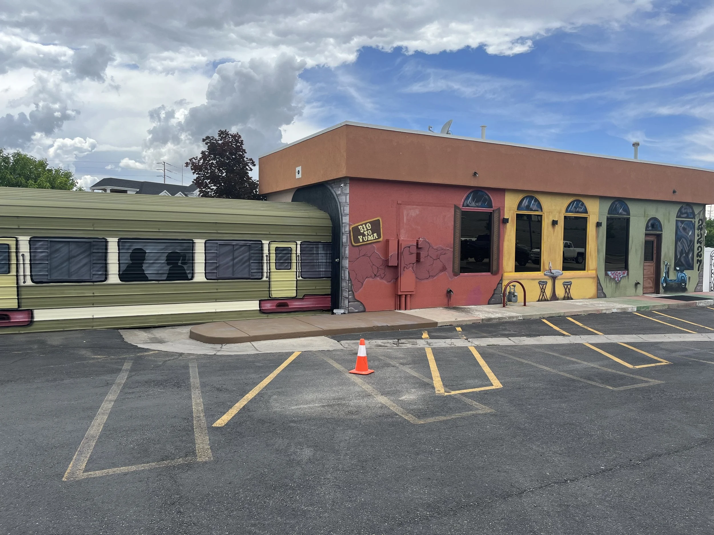 A colorful building with painted walls and large arched windows, featuring decorations and murals, accompanied by a bus and parking lot with traffic cones.