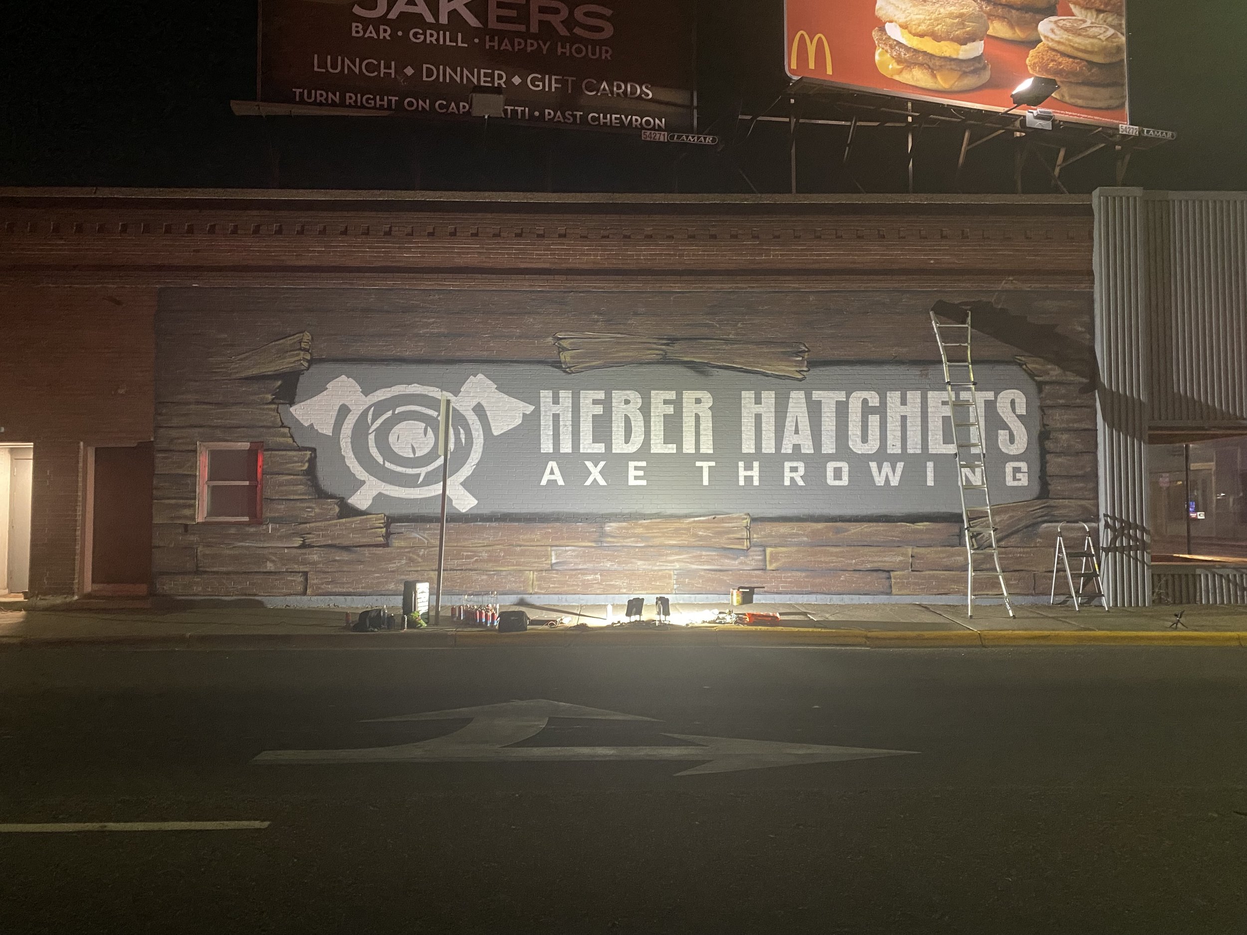 Nighttime exterior view of the Heber Hats Axe Throwing business with a large sign displaying the company logo and name.