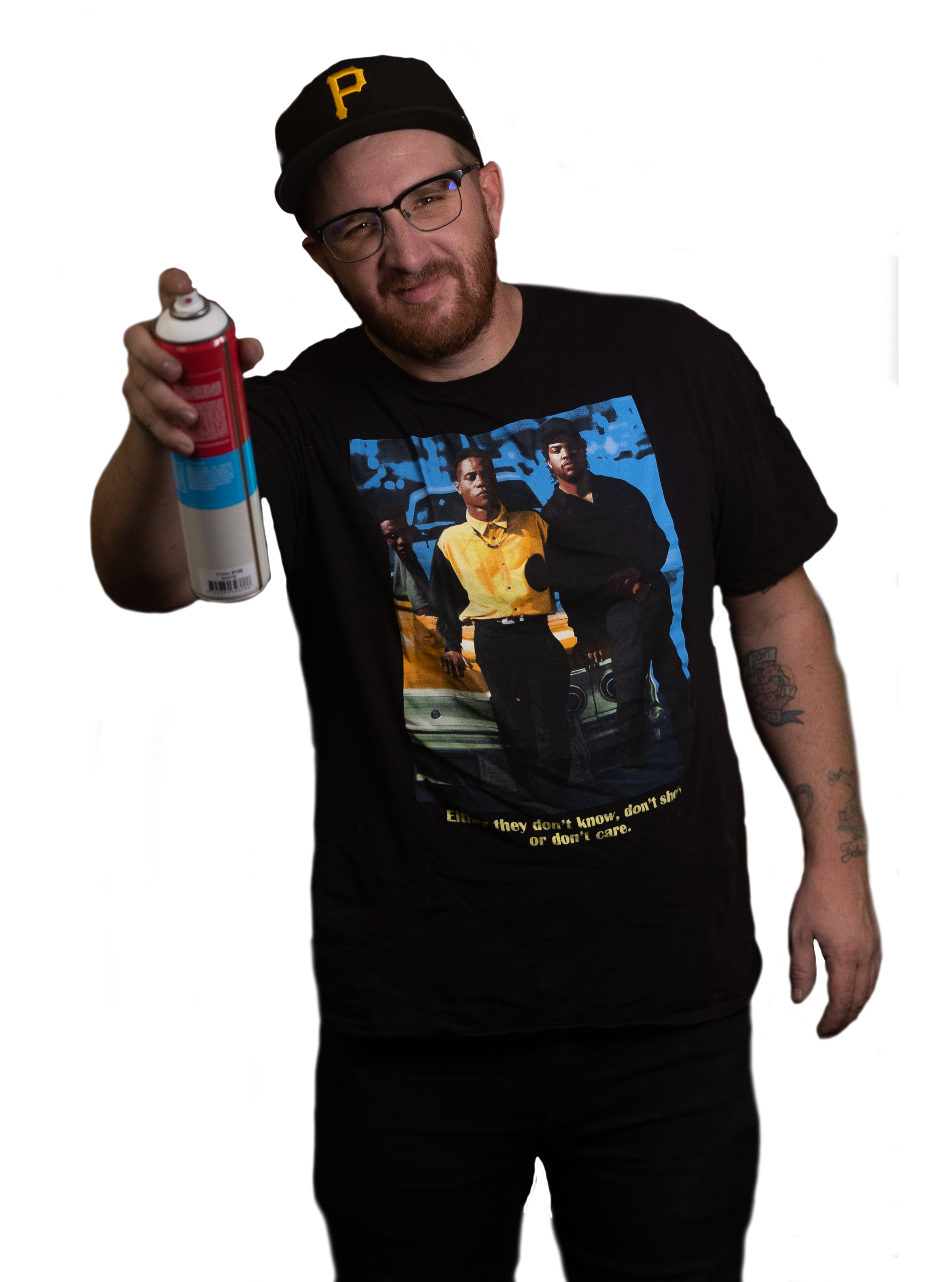 A man wearing a black baseball cap with a yellow 'P', glasses, a beard, and a black t-shirt featuring a group photo, holding a red and white spray can and smiling at the camera.