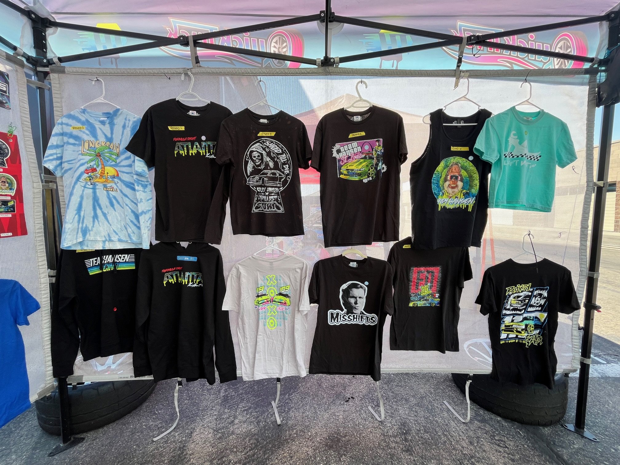 Display of racing-themed T-shirts hanging on a rack at an outdoor event.