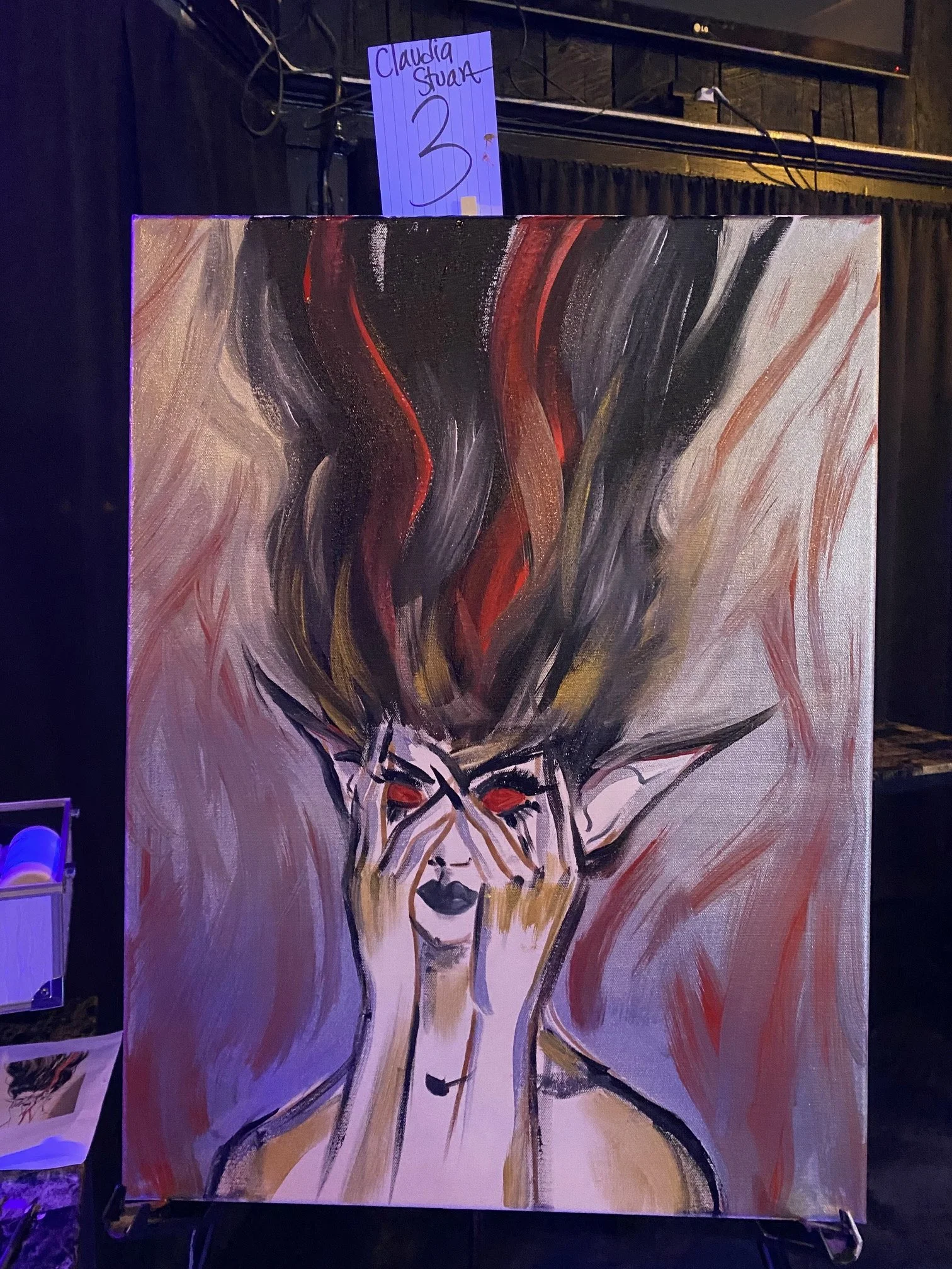 An abstract painting of a woman with closed eyes, black lipstick, with colorful, flowing lines representing hair, on a canvas displayed vertically in an art gallery.