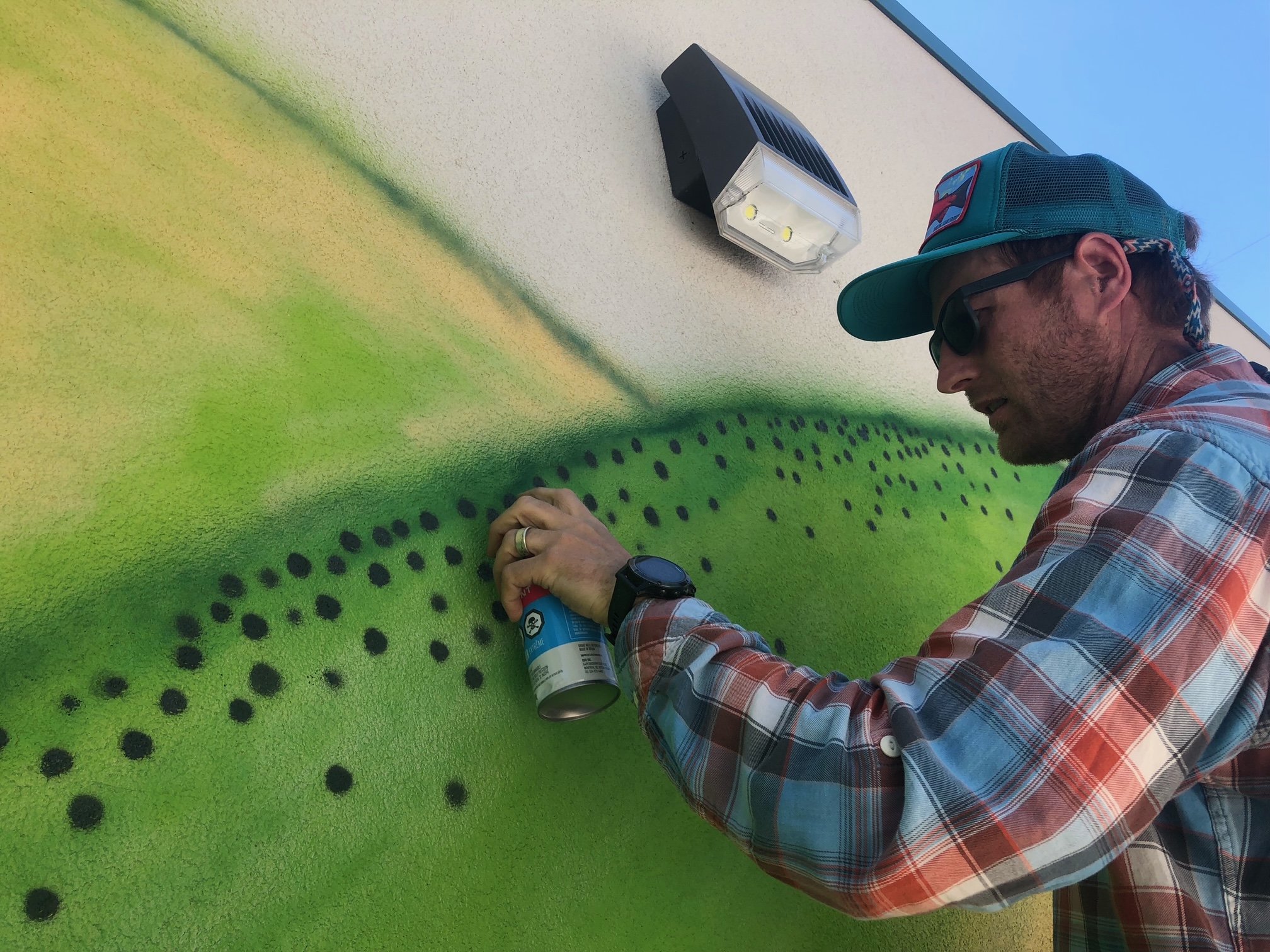 Man spray-painting a wall with green and black spray paint.