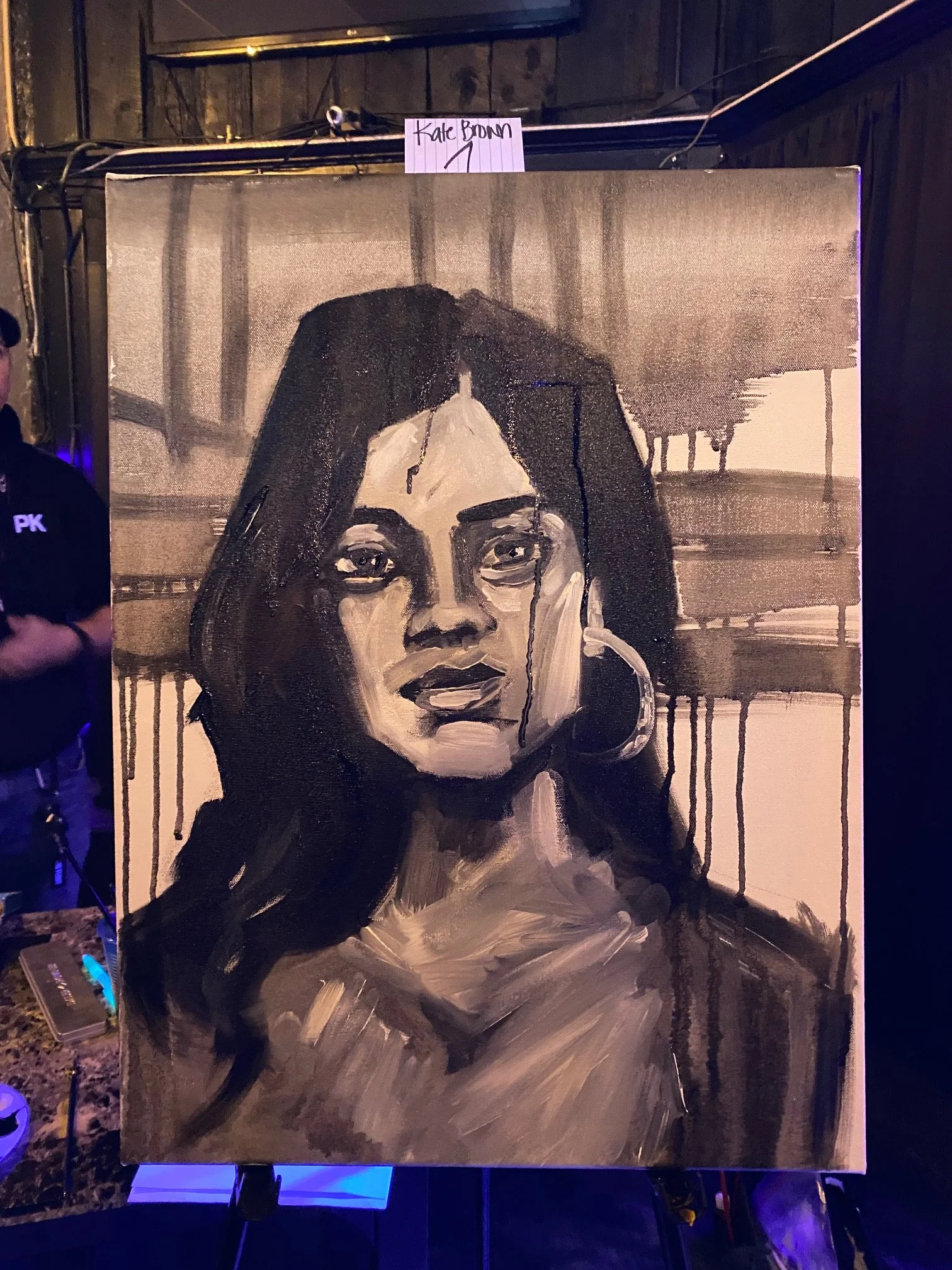 A painting of a woman with dark hair, painted in shades of black, white, and gray. The woman is resting her chin on her hand, with the background featuring a structure with pillars and a horizontal element, possibly a bridge or balcony, with paint dr