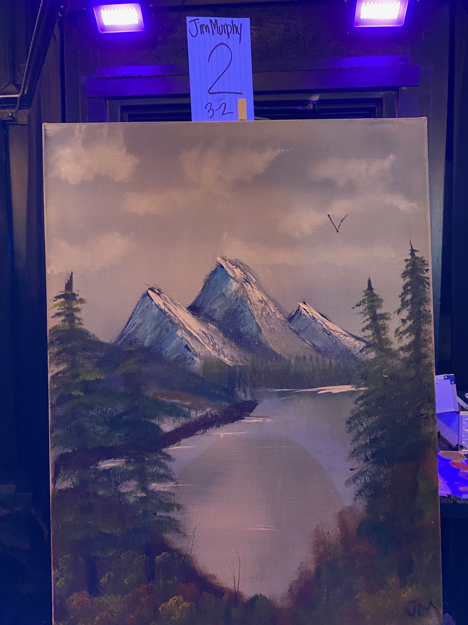 A landscape painting of snow-capped mountain peaks in a forested area with a cloudy sky. The painting is partially obscured by a white note with handwritten text and a seagull illustration.