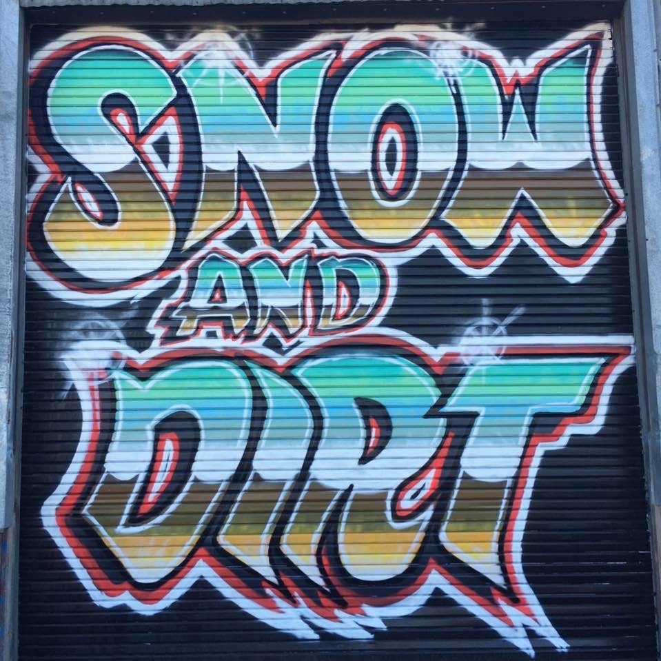 Colorful graffiti art on a metal shutter that reads 'SNOW AND DIRT' with vibrant, outlined letters and a black background.